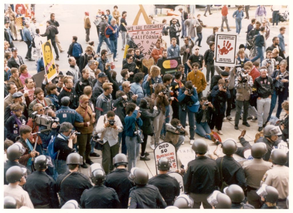 Image of protesters facing police outside FDA building. Sign says, 